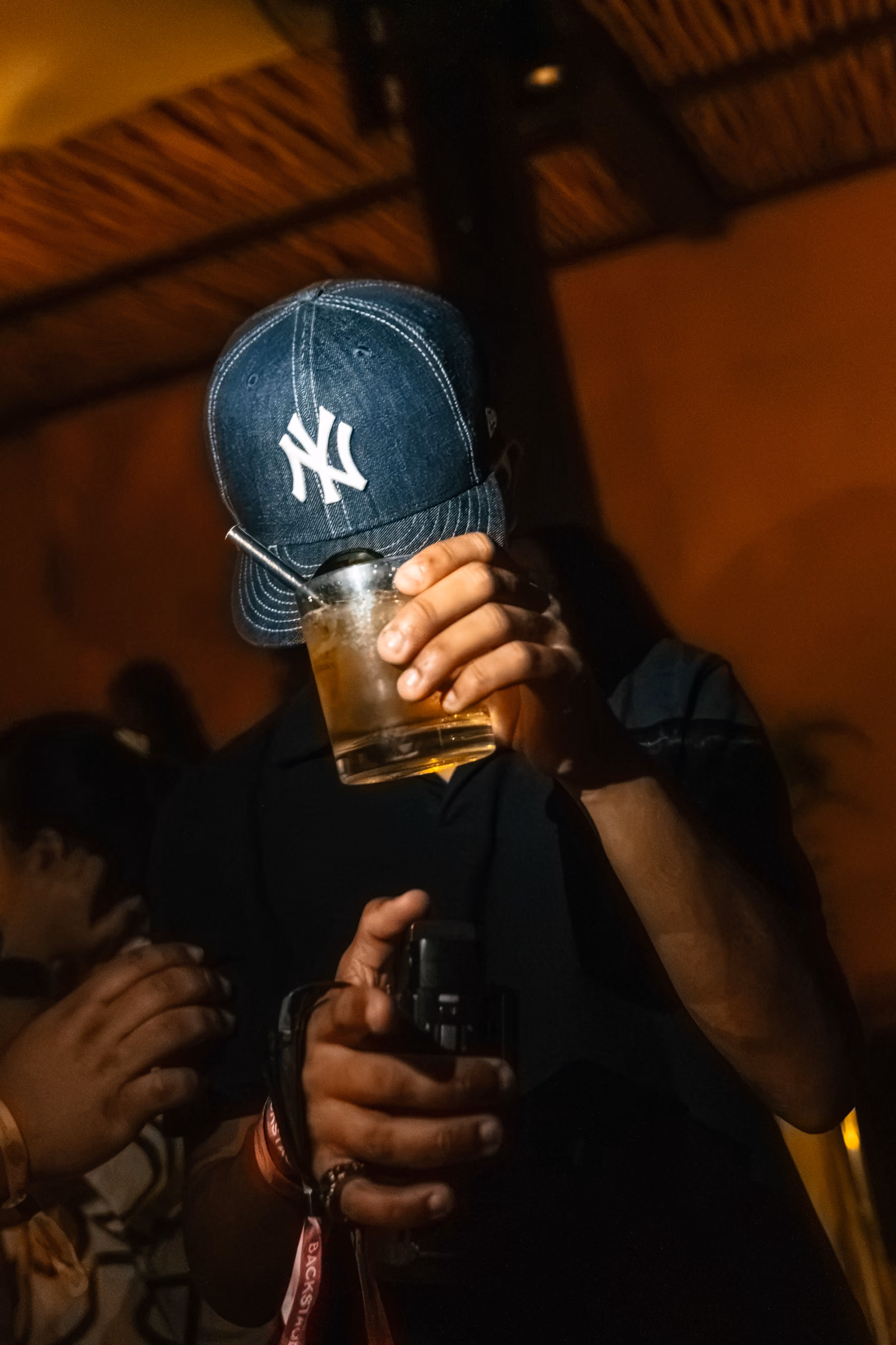 Guest in a New York cap holding a drink at a nighttime event