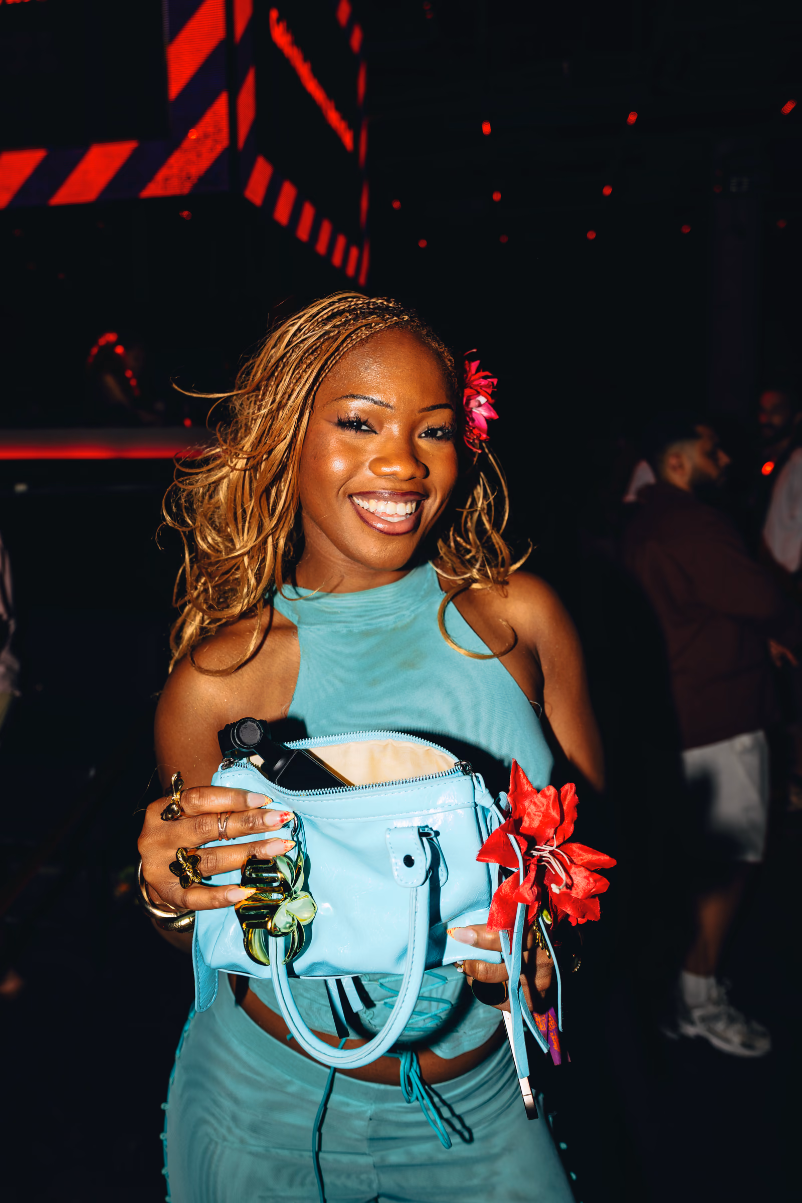 Smiling guest in a teal outfit holding a red flower at an event